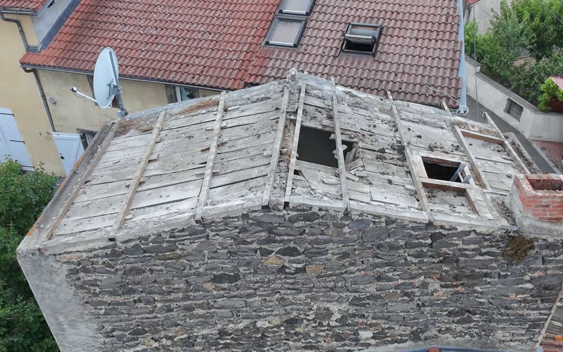Dépose de couverture vue du drone : voliges anciennes mises à nu, planches manquantes, pignon en pierre de lave.