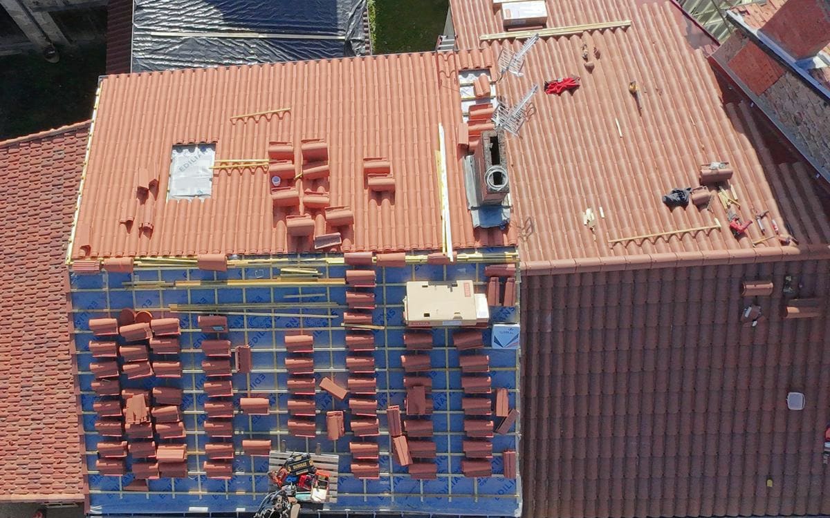 Écran de sous-toiture bleu et contre-lattage posés, tuiles réparties sur le rampant avant pose, vue du drone.