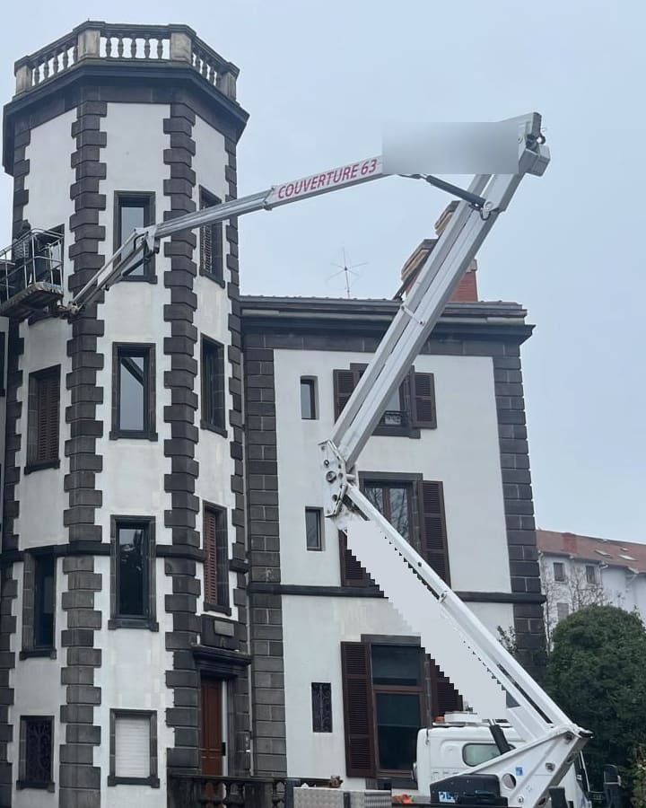 Nacelle de 25 mètres déployée le long de la tour d’un bâtiment en pierre de Volvic, équipe au niveau du faîtage.
