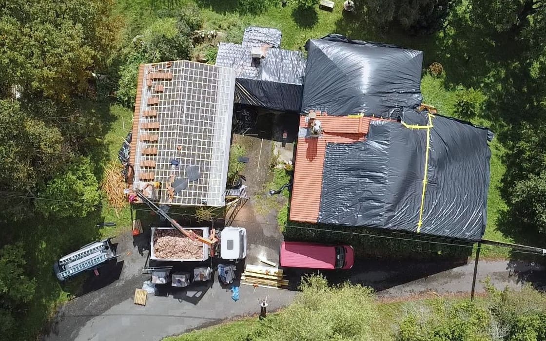 Versant de toiture dégarni sous bâches noires sanglées, benne d’évacuation au pied du bâtiment.