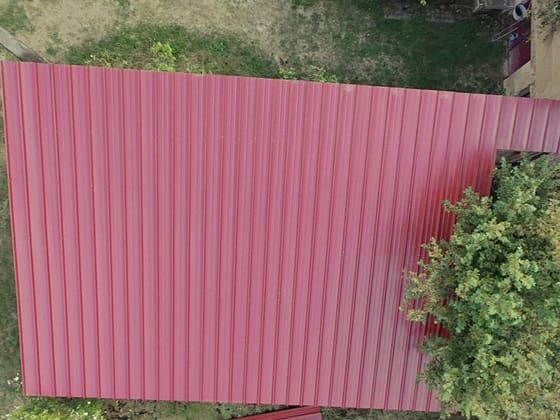 Couverture en bac acier nervuré rouge posée sur un long bâtiment annexe.
