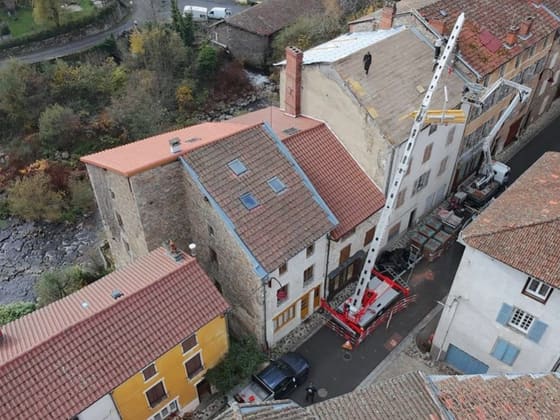 Chantier de couverture en cœur de village vu du drone, monte-matériaux le long de la façade.